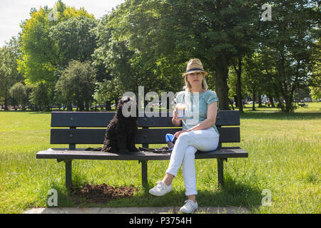 Eine Frau teilt ihr Croissant mit ihrem Hund auf einer Parkbank und genießen Sie einen Kaffee Stockfoto