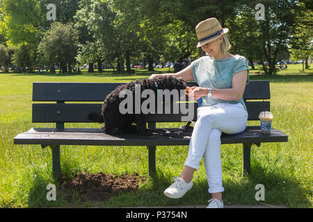 Eine Frau teilt ihr Croissant mit ihrem Hund auf einer Parkbank und genießen Sie einen Kaffee Stockfoto