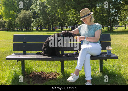 Eine Frau teilt ihr Croissant mit ihrem Hund auf einer Parkbank und genießen Sie einen Kaffee Stockfoto
