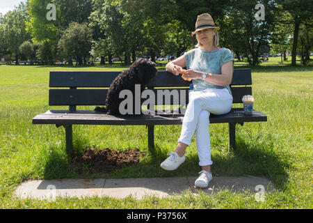 Eine Frau teilt ihr Croissant mit ihrem Hund auf einer Parkbank und genießen Sie einen Kaffee Stockfoto