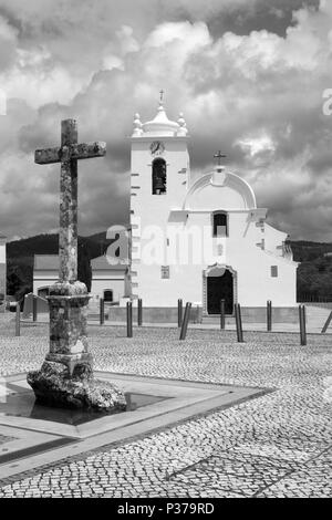 Schwarz-weiß-Bild des Kreuzes und der Kirche auf dem Hauptplatz von Querenca, Portugal Stockfoto
