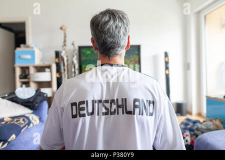 Deutscher fan sitzt in einem Deutschland (Deutschland) Jersey vor einem Fernseher Stockfoto