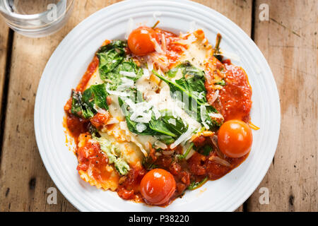 Spinat und Ricotta gefüllte Ravioli in Tomatensauce mit Cherry Tomaten, Pecorino Käse und Pinienkernen Stockfoto