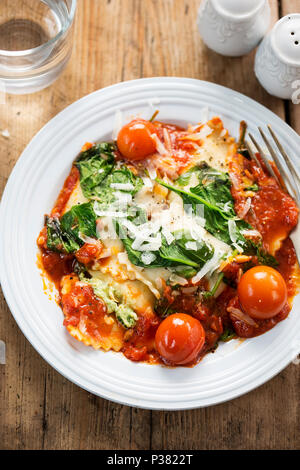 Spinat und Ricotta gefüllte Ravioli in Tomatensauce mit Cherry Tomaten, Pecorino Käse und Pinienkernen Stockfoto