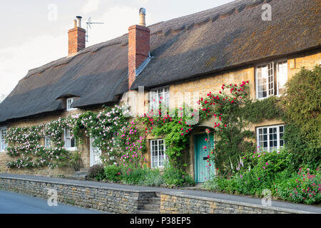 Strohgedeckten Hütten und Kletterrosen in Ebrington, Chipping Campden, Gloucestershire, England Stockfoto