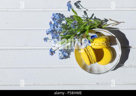 Mehrfarbige Mandel macarons Kekse close-up an der Platte. Frische gelbe Zitrone französische Makronen Gebäck Kekse, Macarons, Makkaroni und Vergißmeinnicht Blumen und leckeres Dessert Stockfoto