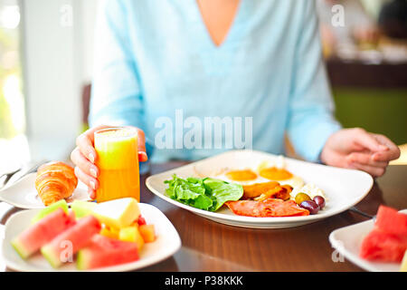 Junge Frau mit Frühstück mit Spiegelei Orangensaft und Obst Stockfoto