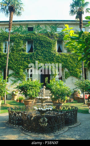 Brunnen und einen kleinen Pool mit kunstvollen schmiedeeisernen Geländer in Garten mit hohen Palmen vor Efeu-coveredTuscan Villa Stockfoto