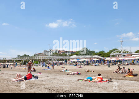 Menschen beim Sonnenbaden auf den Sand vor dem Pier und Restaurant, Blue Moon Beach, Lido di Venezia, die Insel Lido, Venedig, Italien im späten Frühjahr Stockfoto