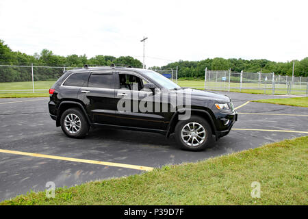 Ein schwarzer Jeep Grand Cherokee sitzen auf einem Parkplatz mit einem Zaun, Bäume, und Stromleitungen in den Hintergrund. Stockfoto