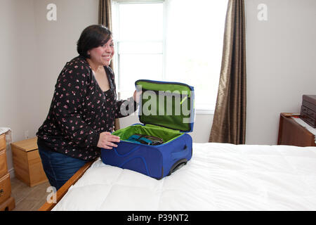 Eine Frau lächelt aufgeregt, als Sie Ihren gepackten Koffer schließt Stockfoto