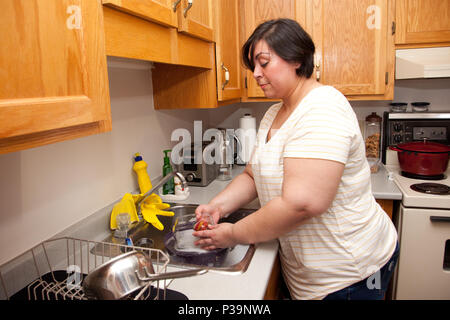 Eine schöne Latina Frau wäscht eine Glasschale in Ihrer Küche zu Hause. Stockfoto