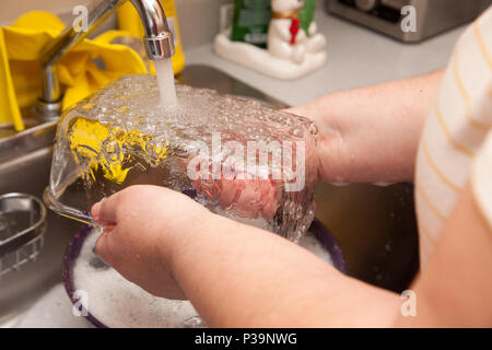 Wasser läuft über ein klares Glas Teller in die Spüle und gewaschen werden Stockfoto
