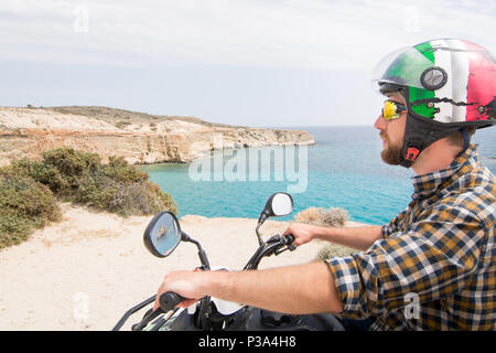 Junger Mann, der Vermietung quad bike auf der Küstenstraße auf der Insel Milos in Richtung Firiplaka Strand, Griechenland Stockfoto