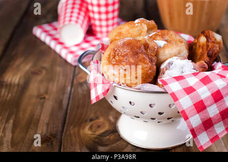 Hausgemachte frittierte Kugeln mit Puderzucker. In red Cage und Glas Serviette. Braun Holz- Hintergrund. Traditionelle Backen Niederlande. Stockfoto