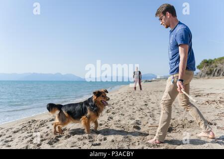 Junge kaukasier männlich spielen mit Hund am Strand. Mensch und Hund Spaß am Meer Stockfoto