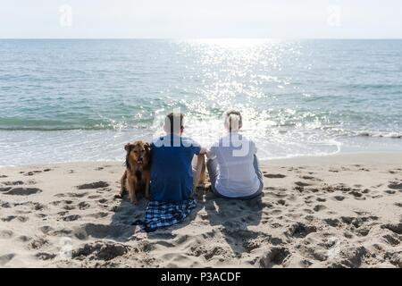 Mutter mit ihrem Sohn und ihrem Hund am Strand den Sonnenuntergang zu beobachten. Stockfoto