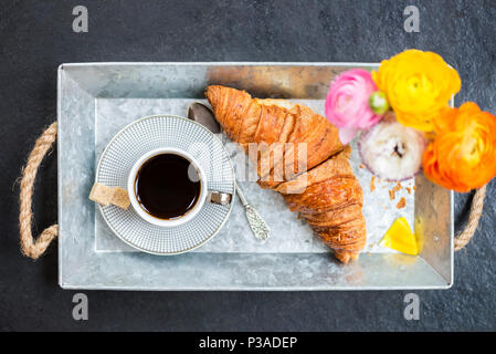 Leichtes Frühstück aus frischen Croissant und Kaffee auf der grauen Fach, Ranunculus Blumen in der Nähe Stockfoto