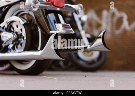 Glänzend verchromt retro Fishtail erschöpft Rohre von Luxus Motorrad. Brick Wall mit Defokussierten Graffiti im Hintergrund. Die sanfte Beleuchtung, Vintage Look Stockfoto