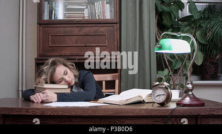 Erschöpft weiblichen schlafend auf dem Stapel der Bücher an ihrem Schreibtisch und durch einen Alarm geweckt gefallen schnell findet ihr Bücher und Papiere, trinkt Kaffee und Blätter Stockfoto