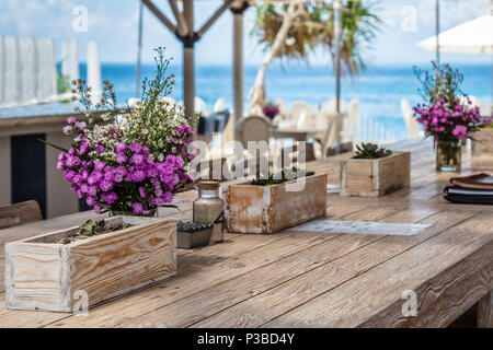 Beach Cafe mit Holztischen und Blumenstrauß, blaues Meer im Hintergrund. Nusa Lembongan, Indonesien Stockfoto