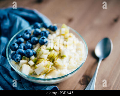 Schüssel mit millet Porridge auf hölzernen Tisch Hintergrund. Organic millet Porridge mit Heidelbeeren und Birne, kopieren Platz für Text. Soft Focus, flacher DOF Stockfoto