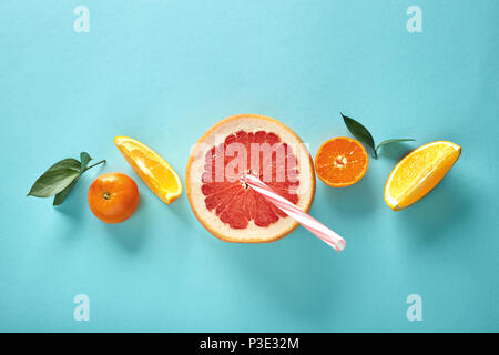 Orangenscheiben und eine Halbe Grapefruit mit einem Strohhalm auf einem blauen Hintergrund in Form eines Musters Stockfoto
