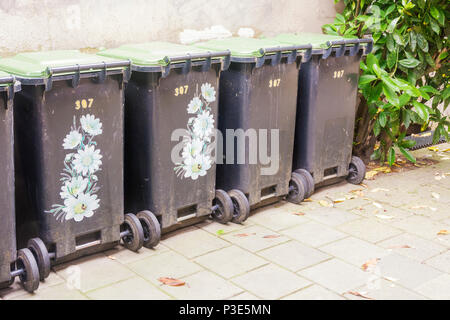 Reihe der Müllcontainer, einige eingerichtet, schön, in der Stadt gegen eine alte Betonwand zu machen. Eine grüne Pflanze neben die Container als na Stockfoto