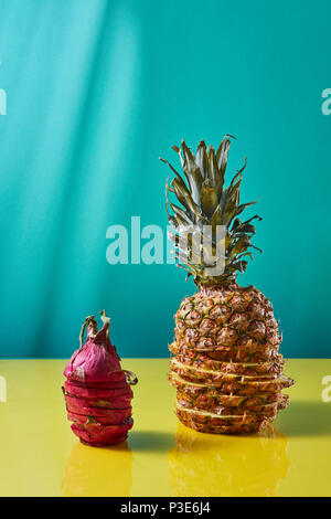 In Scheiben geschnittene Ananas in Scheiben geschnitten und pitaya auf ein blau-gelbes Papier Hintergrund. Exotische Früchte Stockfoto