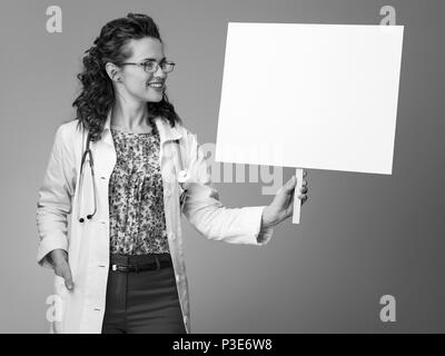 Lächelnd Kinderarzt Frau in Weißem medizinischen Robe an Plakat gegen Hintergrund Stockfoto