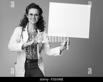 Lächelnd Kinderarzt Frau in Weißem medizinischen Robe an Plakat auf Hintergrund zeigen Stockfoto