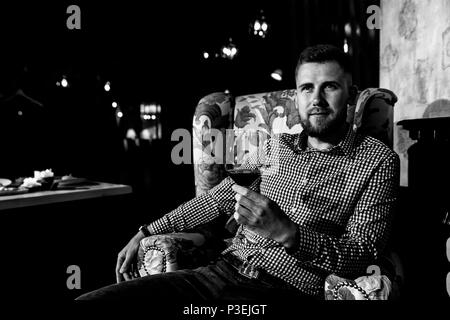 Ein junger Mann sitzt auf einem Stuhl in einem teuren Restaurant, Wein trinken und Stockfoto
