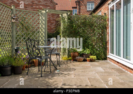 Kleine inländische Garten Terrasse mit Tisch und Stühlen, Natursteinplatten und lackierte Gitter Stockfoto