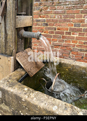 Alte hand Wasserpumpe mit Wasser gießen von der Leitung Rohr über die gartenbewässerung kann in Steintrog. Stockfoto