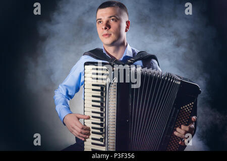 Musiker spielen auf dem Akkordeon vor einem schwarzen Hintergrund. Nebel im Hintergrund. Studio shot Stockfoto