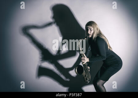 Saxophonist. Frau mit einem Saxophon und eine Silhouette, die auf eine Wand Stockfoto