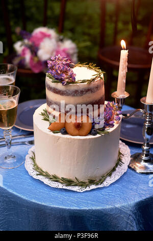 Romantische Hochzeit Abendessen, im Park am Wasser. Viel Grün. Schöne weiße tiered Kuchen mit Blumen und einem pflaumenbaum eingerichtet. Hochzeit Dekor Stockfoto