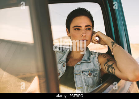 Frau auf einer Reise in einem Auto. Frau mit Tattoos auf Arme, die aus ihrem Auto am Fenster sitzen. Stockfoto