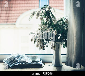 Schale auf einem Stapel Zeitschriften an Fenster mit Vase und Blumen. Sommer noch leben. Gemütlich zu Hause Szene, Lifestyle Stockfoto