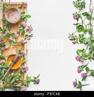 Frische Sommer Honig Konzept. Glas Glas mit Honig, honey comb und Pendelarm auf weißem Hintergrund mit wild wachsenden Blumen, Ansicht von oben, flach, Rahmen. Layout für h Stockfoto