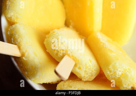 Overhead Nahaufnahme von gelb Ananas Eis am Stiel mit Holzstäbchen, invertiert und in einer weißen Schüssel gruppiert. Stockfoto