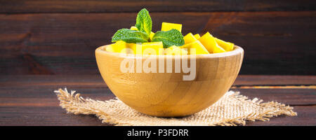Tropische Früchte Mango in einer Platte auf einem hölzernen Hintergrund, ganz oder in Stücken Stockfoto