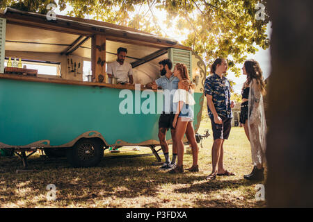 Junge Menschen kaufen Street Food aus einem Lebensmittel Fahrzeug in PARK-Stellung ist. Gruppe von Männern und Frauen, die an der Zugmaschine. Stockfoto