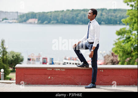 Stilvolle afrikanische amerikanische Geschäftsmann an der Hose und Shirt stellte im Freien gegen See. Stockfoto