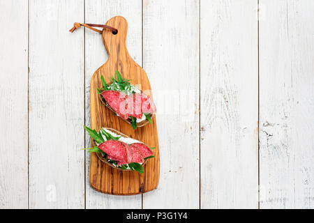 Leckere Vorspeise aus hauchdünn geschnittenem würzige Salami auf Brot mit Käse und Kräutern auf einem Schneidebrett mit Kopie Raum Stockfoto