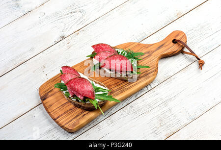 Leckere Vorspeise aus hauchdünn geschnittenem würzige Salami auf Brot mit Käse und Kräutern auf einem Schneidebrett mit Kopie Raum Stockfoto