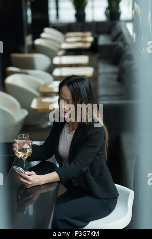 Asiatische Geschäftsfrau mit einem Glas Champagner, während Sie Ihr Mobiltelefon Stockfoto