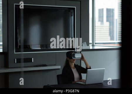 Geschäftsfrau tragen virtual reality Headset während der Arbeit am Laptop Stockfoto