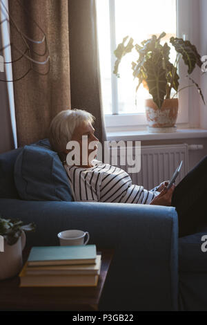Ältere Frau sitzt auf einem Sofa mit Ihrem Tablet-PC im Wohnzimmer Stockfoto