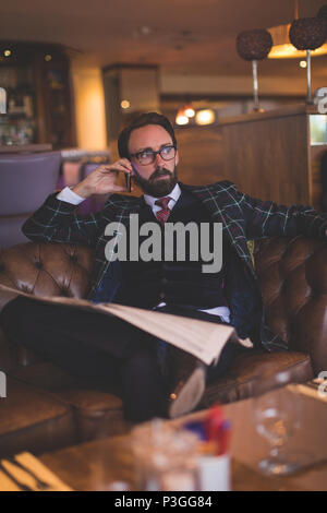 Geschäftsmann mit Mobiltelefon beim Lesen der Zeitung Stockfoto